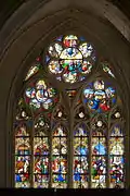 Low-angle view of the Virgin's stained glass window with six sections above with numerous figures and three rosettes above.