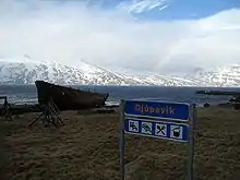 View of the Djúpavík village sign and the wreck of the Suðurland freight ship with Ingólfsfjörður in the background.