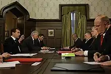 A group of men wearing suits, including Medvedev, sit at a conference table.