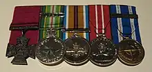 A row of five medals with the Victoria Cross on the left; the other four medals are circular with multicoloured ribbons.