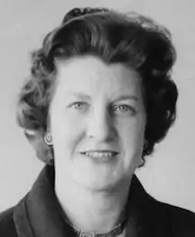 A smiling middle-aged white woman with coiffed dark hair, wearing a dark suit