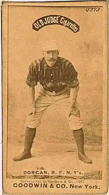 A baseball player standing facing the camera with his hands resting on his knees