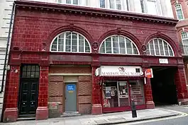 Station building faced in red glazed blocks with three large semi-circular windows at first floor level. Part of the ground floor is occupied by a shop and part has been bricked-up with a small service door