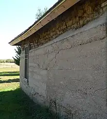 View of wall, with concrete coating lower three-quarters; exposed sod blocks above that