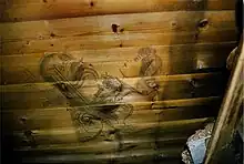  A wooden planked wall on which can be seen a stylised drawing of a woman's head and other ornamental shapes and objects