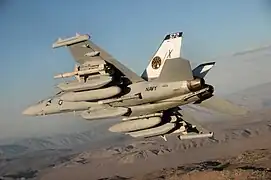 An EA-18G Growler, carrying under each wing an external fuel tank, a AN/ALQ-99 system with a ram air turbine, a jamming pod, and an AGM-88C HARM anti-radiation missile, with an additional AN/ALQ-99 system centered under the fuselage of the aircraft