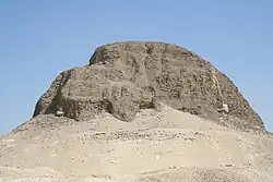 Pyramid sitting on a rocky outcropping. Large portions of the pyramid are missing.