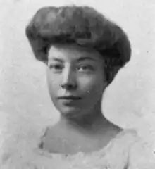 A young white woman with dark hair in a bouffant updo, wearing a white dress with a square ruffled neckline