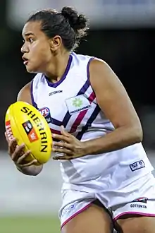 A female athlete with dark hair in a bun holding a football