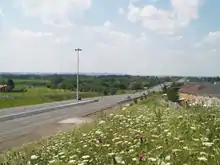 A freeway changes into a four-lane conventional road, and vanishes into the rural foothills