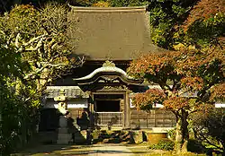 A wooden building behind a roofed wall with a small Chinese style gate.