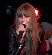 A woman wearing a black jacket singing into a microphone.