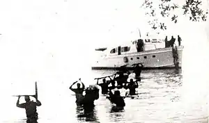 Cuban guerrillas holding rifles above their heads as they wade through the sea, having disembarked from a small boat