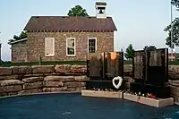 Small memorial of black granite with a one-room schoolhouse in background