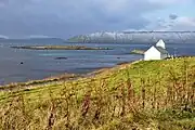 Islet of Kirkjubøhólmur and Saint Olav's Church. Island of Hestur in the distance