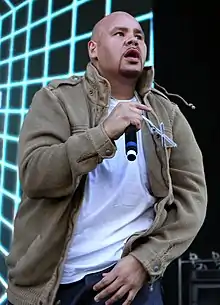 A large man on stage with a microphone in his right hand and blue lights behind him.