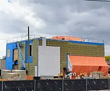 Photo of a light rail and subway station entrance under construction. White cladding panels have been affixed to a small portion of the exterior.