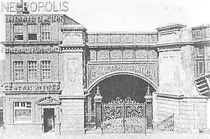 Three-story office building next to a railway arch, with an ornate gate in front of it.