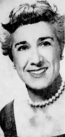 Portrait of a smiling short-haired woman in a dark square-necked dress wearing a pearl choker.