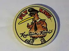 Promotional button for Kiwi International Airlines, circa 1994. Diameter 54mm. Yellow background, with cartoon figure of a Kiwi bird wearing airline captain's hat, tie, wings, and shoulder insignia.  Says "FLY WIKI" in red block letters on the top, and "Kaptain Kiwi" in script across the bottom.