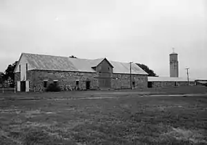 A black and white picture of a long two story Quartermaster store building made of yellowish cut stone with a wooden second floor. The building is in the style of the late 1860s.