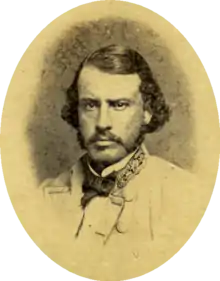 Sepia toned oval photo shows a mustachioed man looking hard at the camera. He wears a light-colored uniform with the stars of a general on his collar.