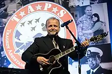 Musician Frank J. Myers, playing an acoustic guitar and singing into a microphone.