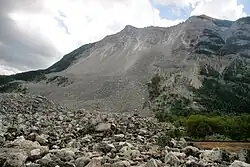 Side view of a mountain scarred by a large debris field down its side. A field of rock lies at its base.