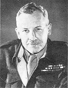 Head and shoulders of man with a moustache wearing battledress jacket and ribbons with a shirt and tie.