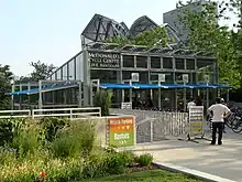 A glass building beyond landscaping with signs pointing to downstairs facilities and a sign reading "McDonald's Cycle Center 239 E. Randolph" with people in the building and in front of it