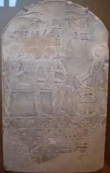 A stone stela with raised-relief images of a man seated with his son and wife, while a man stands to the right giving libations; Egyptian hieroglyphs are written in distinctly-marked horizontal columns at the bottom portion of the stela.