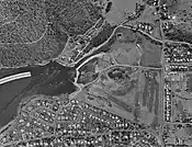 Geilston Bay, Tasmania, aerial photograph 24 Jan 1969. Note that development has now occurred on the southern flank of the Bay. The curved white object is a portion of the arch of the former Hobart floating bridge, in storage pending its removal, following the opening of its replacement, the Tasman Bridge, which opened in August 1964. The central, undeveloped area is now occupied by, among others, the Boat Club buildings and the Lindisfarne Golf Course, while the former quarry workings are still visible.