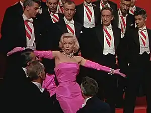 Marilyn Monroe in a pink gown, surrounded by men in tuxedos