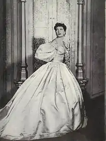 Woman looking over her shoulder, wearing a Victorian-style gown with a fitted bodice and full hoop skirt