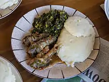 A meal of sadza (right), greens, and goat offal.  The goat's small intestines are wrapped around small pieces of large intestines before cooking.