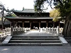 A short, wide, two-story building with a large bridge in front of it. The front of the building is supported by eight support exposed columns. The first and second stories each have separate, curved roofs, with the top roof curving upwards sharply and the bottom roof curving gradually.