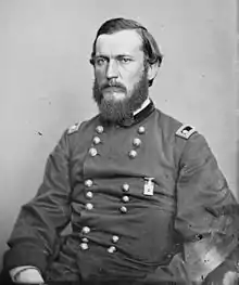 Black and white photo shows a serious-looking man with a beard. He wears a dark military uniform with two rows of buttons and the two-star shoulder tabs of a major general.