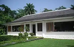 a single story white building with a grey roof and palm trees in the background