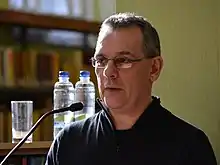 This image shows Graham Allen standing at a podium in the Cork City Libraries, reading at the launch of his first collection of poetry, The One That Got Away.