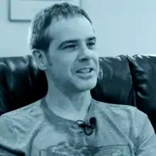 A blue duotone headshot photo of a white man with a short haircut in T-shirt