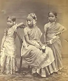 Image 10A Tamil Hindu girl (center) in 1870 wearing a half-saree, flowers and jewelry from her Ritu Kala samskara rite of passage (from Samskara (rite of passage))