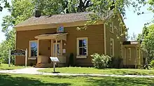 A yellow, wooden building, with a sign out front identifying it as Guy House