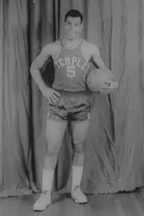 A man, wearing a jersey with a word "TEMPLE" and the number "5" written in the front, is holding a basketball while posing for a photo