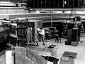 HD.6B.437 - A view of the inside of the Cosmotron ring showing engineer working or high level power amplifier. The orderly assembly of tubes and hoses to the left is a portion of the waterflow interlock system.