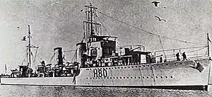 Three-quarter front view of destroyer with twin funnels and two forward gun turrets, at sea