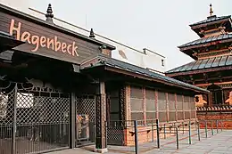 Photograph of a caged building behind a fence. Atop the gates are metal silhouettes of elephants. On the right side of the photograph is a 3-storey pagoda.