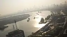 A curving river at dusk lit with diffuse light. Ships and docks can be seen on the river