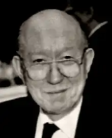 Elderly, clean-shaven man in suit and spectacles.