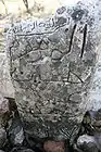 Close up view of the inscription of a rock that does not seem to have been worked on by a stonemason, given its irregular shape and unsmoothed surface.