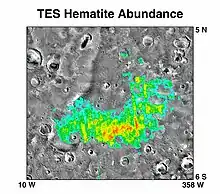 A grayscale map of an area on Mars (from 5° N to 6° S and from 10° W to 358° W (or 2° E), crossing 0° in both axes), with a false-color overlay (cyan, green, yellow, red) showing hematite abundance on the surface.